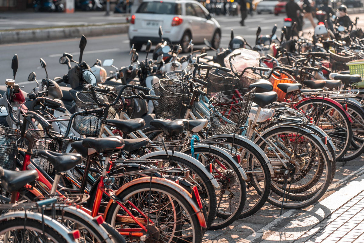 Row of bicycles parked along a busy urban sidewalk under sunlight.