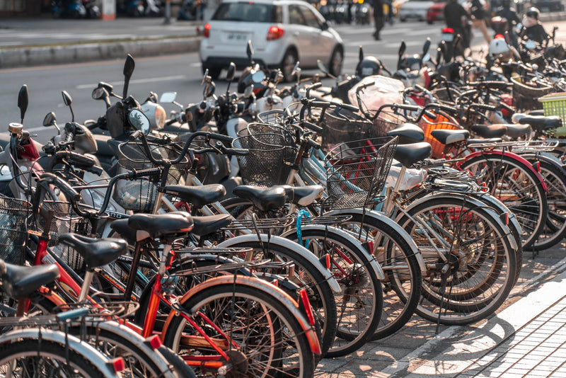 Row of bicycles parked along a busy urban sidewalk under sunlight.