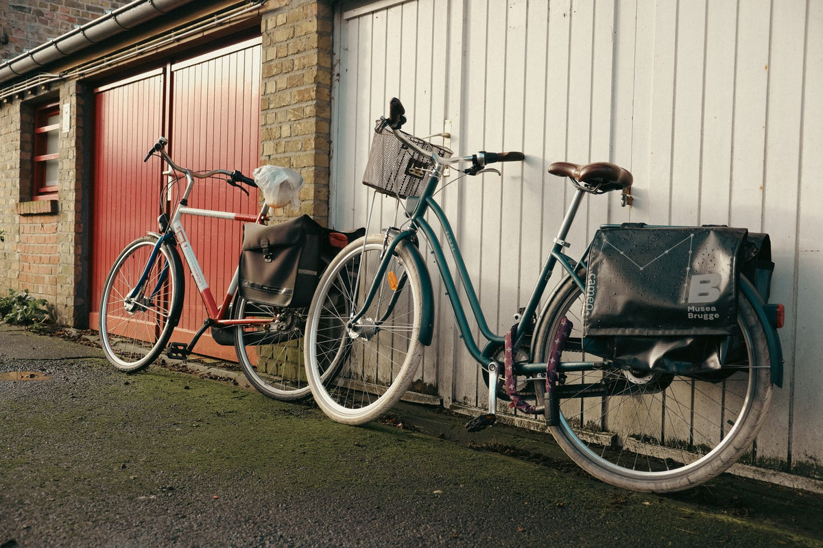 Two vintage bicycles parked against a brick and wood garage exterior.