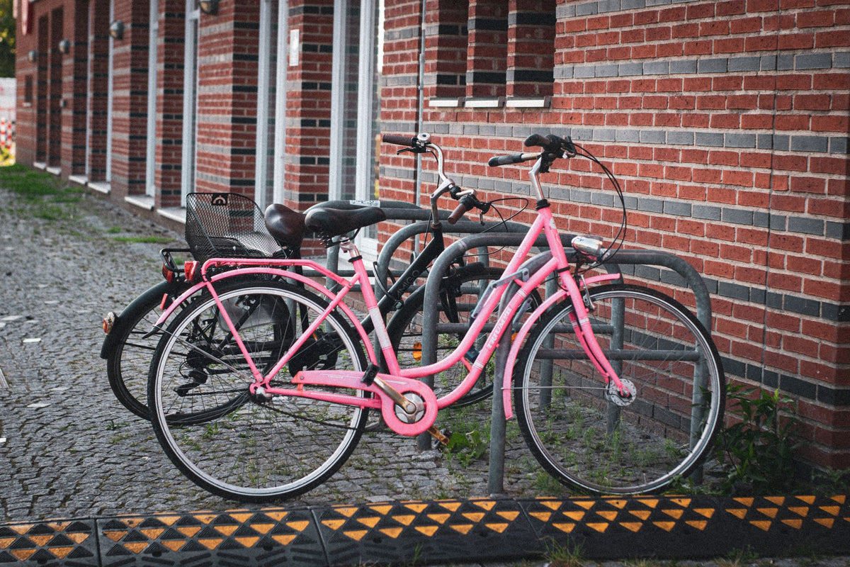Two bicycles, one bright pink, parked in front of brick wall in Bremen, Germany.