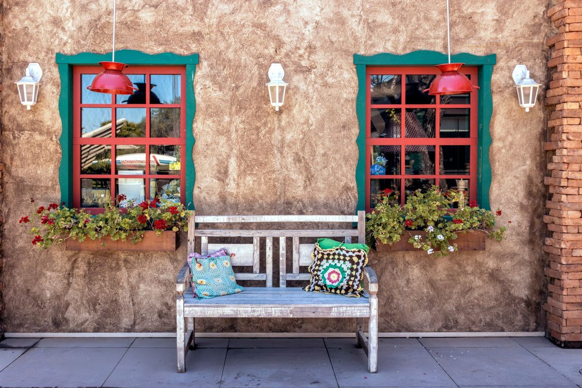 Cozy rustic facade with green-trimmed windows, wooden bench, and colorful flower pots.