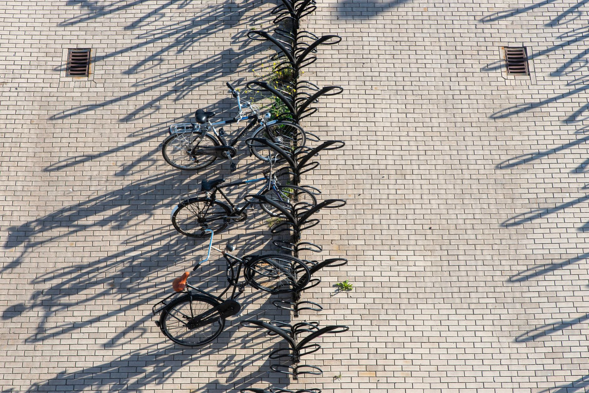 A top-down view of a bicycle stand casting long shadows on a sunny paved area.