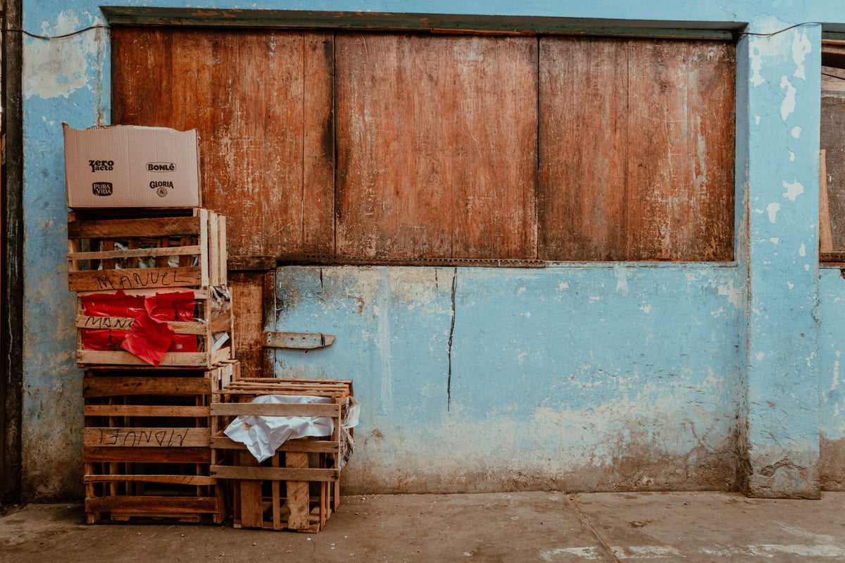 Stack of wooden crates and boxes against a weathered blue wall in Pacasmayo, Peru.